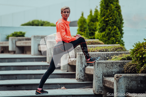 Image of Fit attractive woman in sportswear stretching one leg before jogging on the footpath outdoor in summer among greenery. Workout, sport, activity, fitness, vacation and training concept.