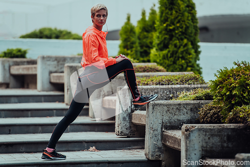 Image of Fit attractive woman in sportswear stretching one leg before jogging on the footpath outdoor in summer among greenery. Workout, sport, activity, fitness, vacation and training concept.