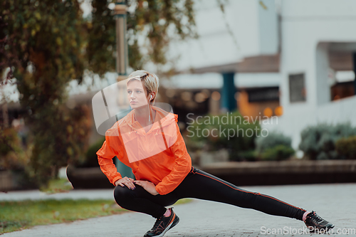 Image of Fit attractive woman in sportswear stretching one leg before jogging on the footpath outdoor in summer among greenery. Workout, sport, activity, fitness, vacation and training concept.