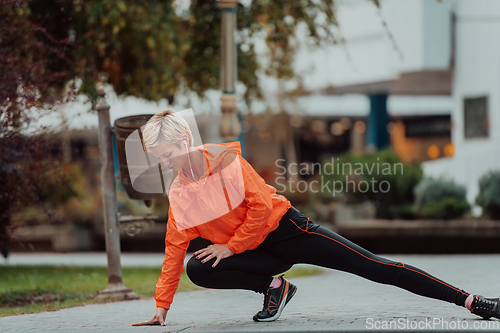 Image of Fit attractive woman in sportswear stretching one leg before jogging on the footpath outdoor in summer among greenery. Workout, sport, activity, fitness, vacation and training concept.