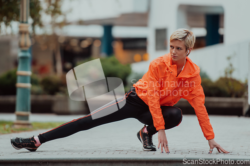 Image of Fit attractive woman in sportswear stretching one leg before jogging on the footpath outdoor in summer among greenery. Workout, sport, activity, fitness, vacation and training concept.