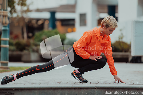 Image of Fit attractive woman in sportswear stretching one leg before jogging on the footpath outdoor in summer among greenery. Workout, sport, activity, fitness, vacation and training concept.