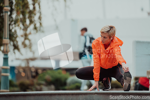 Image of Fit attractive woman in sportswear stretching one leg before jogging on the footpath outdoor in summer among greenery. Workout, sport, activity, fitness, vacation and training concept.