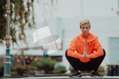 Image of Fit attractive woman in sportswear stretching one leg before jogging on the footpath outdoor in summer among greenery. Workout, sport, activity, fitness, vacation and training concept.