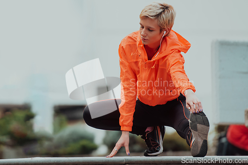 Image of Fit attractive woman in sportswear stretching one leg before jogging on the footpath outdoor in summer among greenery. Workout, sport, activity, fitness, vacation and training concept.