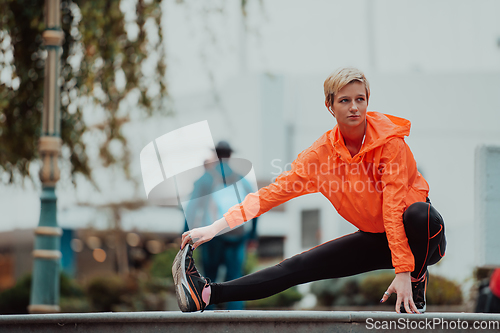 Image of Fit attractive woman in sportswear stretching one leg before jogging on the footpath outdoor in summer among greenery. Workout, sport, activity, fitness, vacation and training concept.