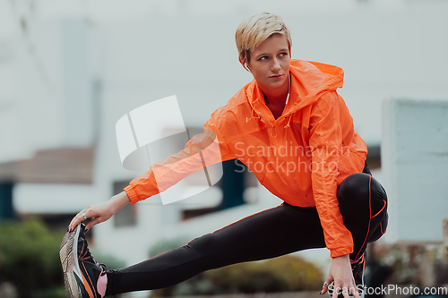 Image of Fit attractive woman in sportswear stretching one leg before jogging on the footpath outdoor in summer among greenery. Workout, sport, activity, fitness, vacation and training concept.