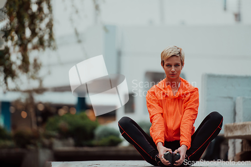 Image of Fit attractive woman in sportswear stretching one leg before jogging on the footpath outdoor in summer among greenery. Workout, sport, activity, fitness, vacation and training concept.