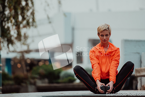 Image of Fit attractive woman in sportswear stretching one leg before jogging on the footpath outdoor in summer among greenery. Workout, sport, activity, fitness, vacation and training concept.