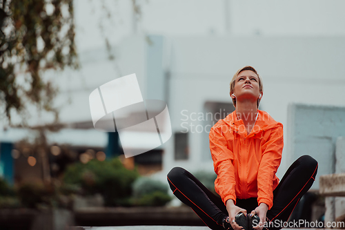 Image of Fit attractive woman in sportswear stretching one leg before jogging on the footpath outdoor in summer among greenery. Workout, sport, activity, fitness, vacation and training concept.