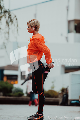 Image of Fit attractive woman in sportswear stretching one leg before jogging on the footpath outdoor in summer among greenery. Workout, sport, activity, fitness, vacation and training concept.