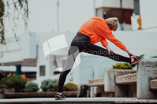 Image of Fit attractive woman in sportswear stretching one leg before jogging on the footpath outdoor in summer among greenery. Workout, sport, activity, fitness, vacation and training concept.