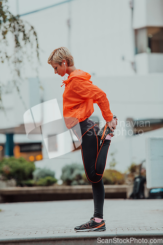 Image of Fit attractive woman in sportswear stretching one leg before jogging on the footpath outdoor in summer among greenery. Workout, sport, activity, fitness, vacation and training concept.