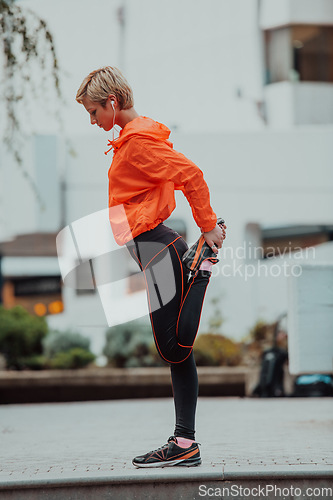 Image of Fit attractive woman in sportswear stretching one leg before jogging on the footpath outdoor in summer among greenery. Workout, sport, activity, fitness, vacation and training concept.