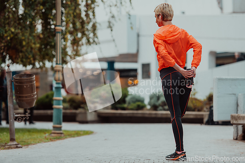 Image of Fit attractive woman in sportswear stretching one leg before jogging on the footpath outdoor in summer among greenery. Workout, sport, activity, fitness, vacation and training concept.