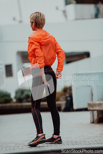 Image of Fit attractive woman in sportswear stretching one leg before jogging on the footpath outdoor in summer among greenery. Workout, sport, activity, fitness, vacation and training concept.