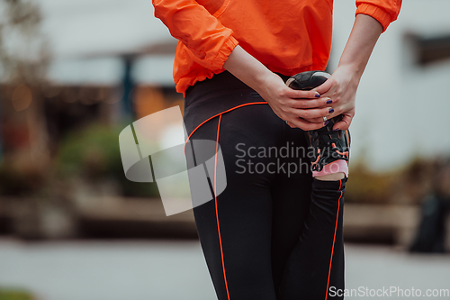 Image of Fit attractive woman in sportswear stretching one leg before jogging on the footpath outdoor in summer among greenery. Workout, sport, activity, fitness, vacation and training concept.