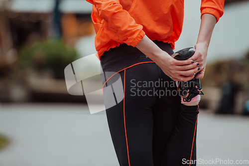 Image of Fit attractive woman in sportswear stretching one leg before jogging on the footpath outdoor in summer among greenery. Workout, sport, activity, fitness, vacation and training concept.