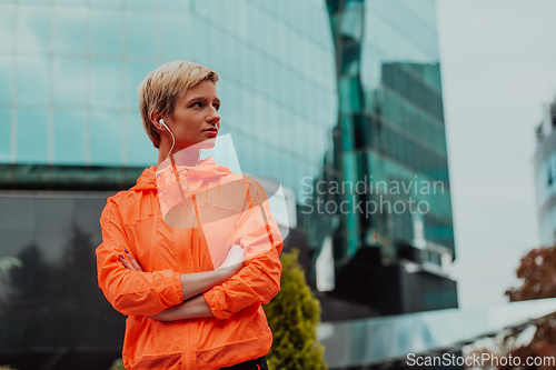 Image of a woman in a sports outfit is resting in a city environment after a hard morning workout while using noiseless headphones