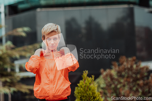 Image of a woman in a sports outfit is resting in a city environment after a hard morning workout while using noiseless headphones