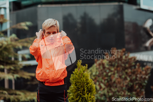 Image of a woman in a sports outfit is resting in a city environment after a hard morning workout while using noiseless headphones