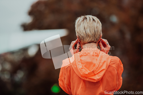 Image of a woman in a sports outfit is resting in a city environment after a hard morning workout while using noiseless headphones