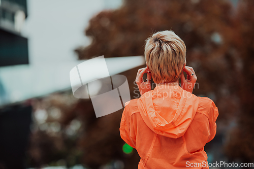 Image of a woman in a sports outfit is resting in a city environment after a hard morning workout while using noiseless headphones