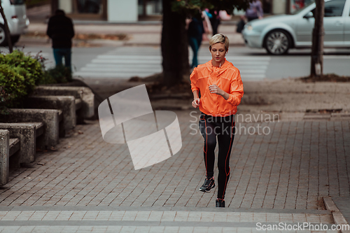 Image of A blonde in a sports outfit is running around the city in an urban environment. The hot blonde maintains a healthy lifestyle.