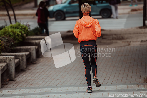 Image of A blonde in a sports outfit is running around the city in an urban environment. The hot blonde maintains a healthy lifestyle.