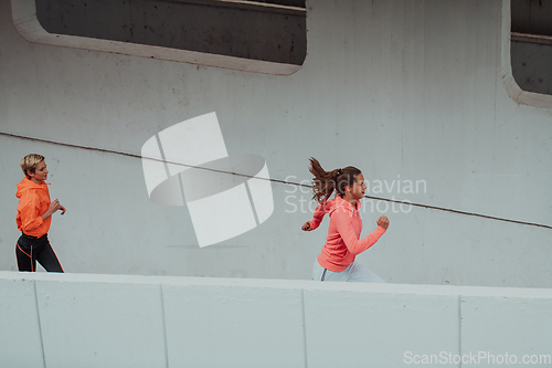 Image of Two women in sports clothes running in a modern urban environment. The concept of a sporty and healthy lifestyle