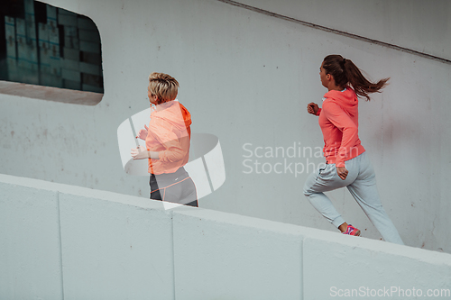 Image of Two women in sports clothes running in a modern urban environment. The concept of a sporty and healthy lifestyle