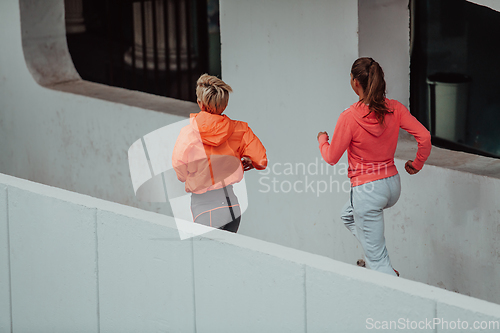 Image of Two women in sports clothes running in a modern urban environment. The concept of a sporty and healthy lifestyle