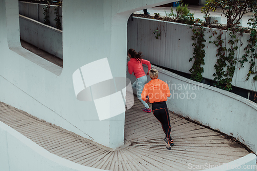 Image of Two women in sports clothes running in a modern urban environment. The concept of a sporty and healthy lifestyle