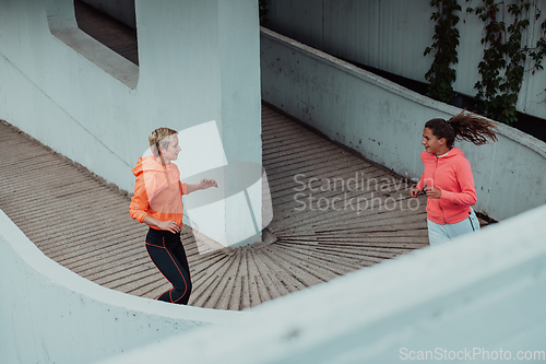 Image of Two women in sports clothes running in a modern urban environment. The concept of a sporty and healthy lifestyle