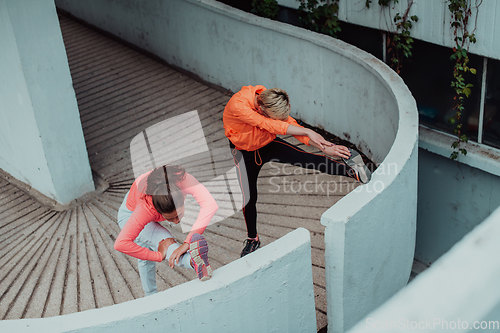 Image of Two women warming up together and preparing for a morning run in an urban environment. Selective focus