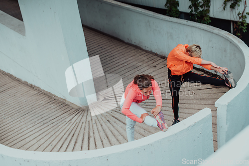 Image of Two women warming up together and preparing for a morning run in an urban environment. Selective focus