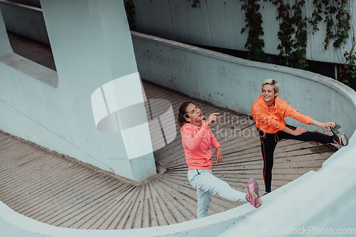 Image of Two women warming up together and preparing for a morning run in an urban environment. Selective focus