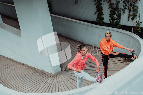 Image of Two women warming up together and preparing for a morning run in an urban environment. Selective focus