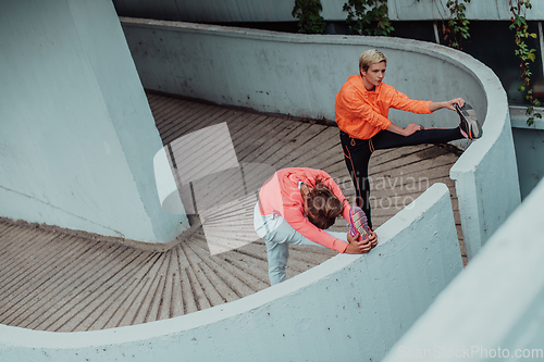 Image of Two women warming up together and preparing for a morning run in an urban environment. Selective focus