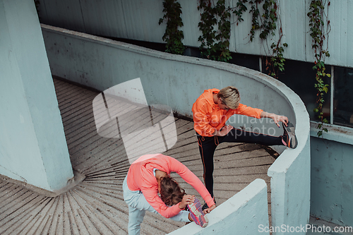 Image of Two women warming up together and preparing for a morning run in an urban environment. Selective focus