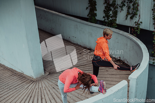 Image of Two women warming up together and preparing for a morning run in an urban environment. Selective focus