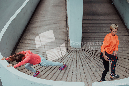 Image of Two women warming up together and preparing for a morning run in an urban environment. Selective focus