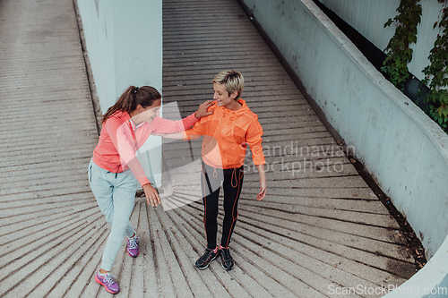 Image of Two women warming up together and preparing for a morning run in an urban environment. Selective focus