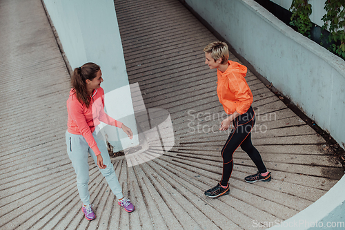 Image of Two women warming up together and preparing for a morning run in an urban environment. Selective focus