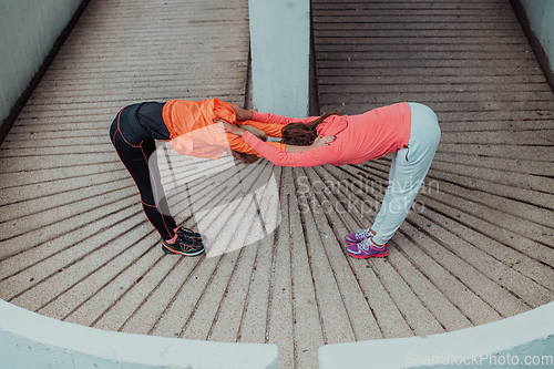 Image of Two women warming up together and preparing for a morning run in an urban environment. Selective focus