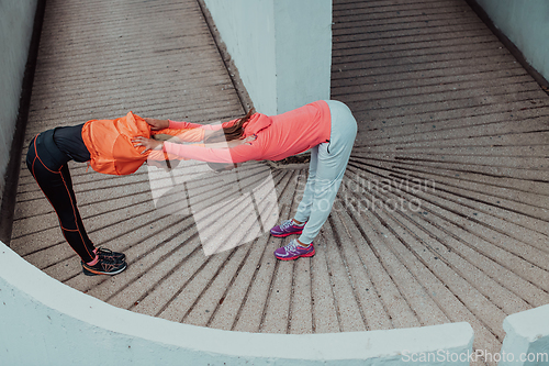 Image of Two women warming up together and preparing for a morning run in an urban environment. Selective focus