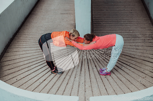 Image of Two women warming up together and preparing for a morning run in an urban environment. Selective focus