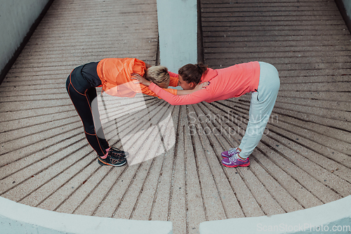 Image of Two women warming up together and preparing for a morning run in an urban environment. Selective focus