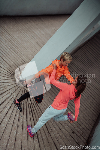 Image of Two women warming up together and preparing for a morning run in an urban environment. Selective focus