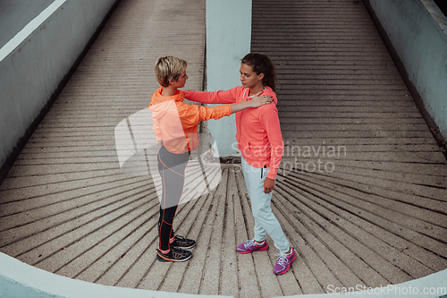 Image of Two women warming up together and preparing for a morning run in an urban environment. Selective focus